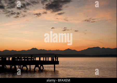 Fotograf auf einen Alki Beach Pier in West Seattle, Washington. Die Sonne geht über die Olympic Mountains und Bainbridge Island. Stockfoto