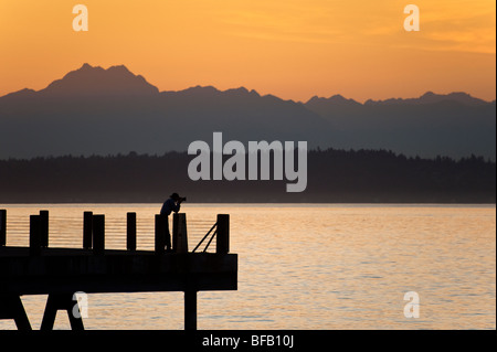 Fotograf auf einen Alki Beach Pier in West Seattle, Washington. Die Sonne geht über die Olympic Mountains und Bainbridge Island. Stockfoto