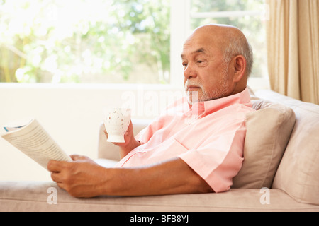 Senior woman Lesebuch mit trinken zu Hause Stockfoto