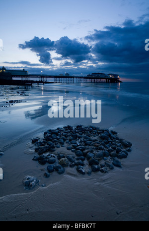 Cromer Pier in der Nacht mit einem Kreis aus Kieselsteinen im Vordergrund. Stockfoto