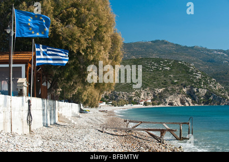 Ein Strand mit Kieselsteinen, Tamarisken und eine Taverne mit der griechischen und europäischen Flagge Stockfoto