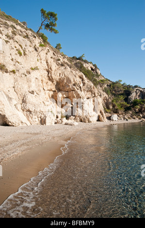 Blick entlang einen kleinen Sandstrand auf einer griechischen Insel mit einem Baum und einige Felsen und Klippen im Hintergrund. Stockfoto