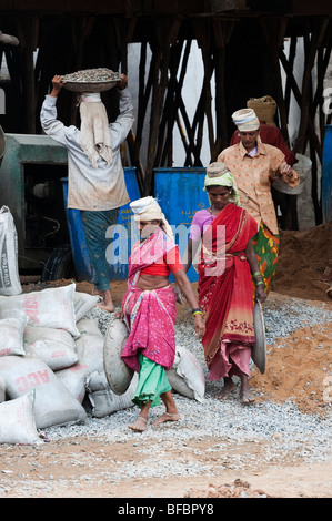 Indische Frauen arbeiten auf der Baustelle, mit Sand und Stein auf dem Kopf in einen Betonmischer zu setzen. Puttaparthi, Andhra Pradesh, Indien Stockfoto