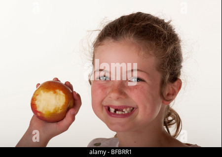 kleines Mädchen (7 Jahre alt), das vorderen Zähne zu essen Apfel auf rote Bohnenbeutelstuhl vor weißem Hintergrund fehlt Stockfoto