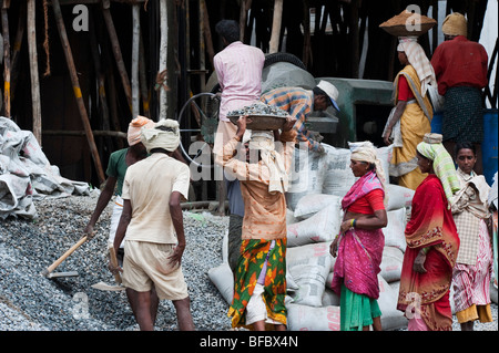 Indische Frauen arbeiten auf der Baustelle, mit Sand und Stein auf dem Kopf, in einen Betonmischer zu setzen. Puttaparthi, Andhra Pradesh, Indien Stockfoto