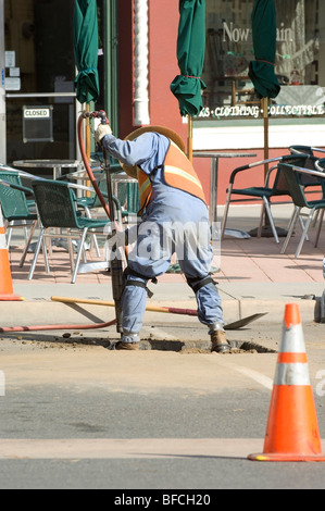 Öffentliche arbeiten Mitarbeiter an einem heißen Tag mit einem Presslufthammer auf der Straße, an den Rohren zu arbeiten, die unter dem Straßenniveau liegen. Stockfoto