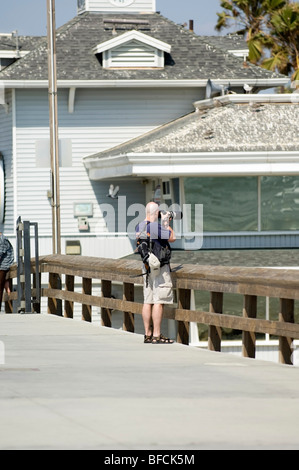 Ein Fotograf, stehend auf dem Newport Beach Pier, hält seine Objektiv und Kamera-Ausrüstung stetig um den perfekten Schuss Stockfoto
