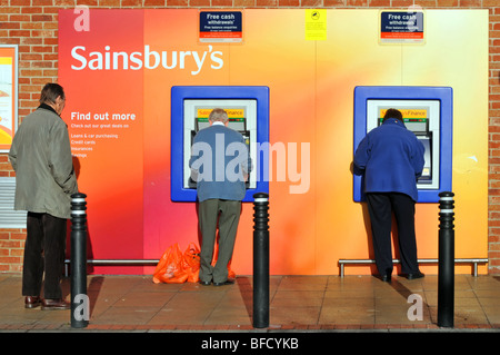 Mann und Frau ein Mann warten Sainsburys ATM mit Stockfoto