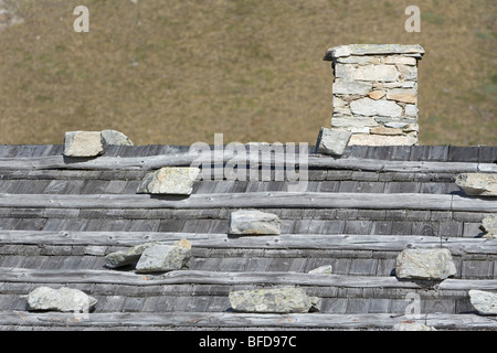 Traditionelle Berg Hütte Dach und Schornstein, Steinen gedrückt halten der hölzernen Fliese oder Schindeldach. Italienische Alpen Stockfoto