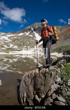 Eine Backpacker steht auf einem Felsvorsprung über dem See mit Wanderstöcken in Colorado. Stockfoto