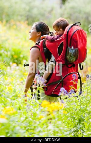 Mutter trägt Kind im Rucksack. Wildblumenwiese. Backpacking in Maroon Bells Snowmass Wildnis außerhalb von Aspen Colorado Stockfoto