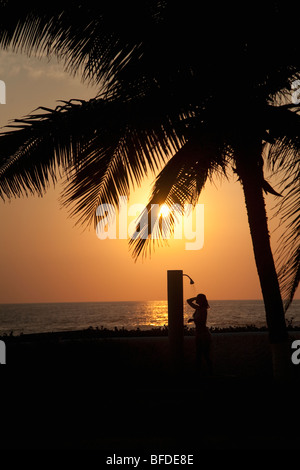 Eine Frau, die direkt am Meer unter Palmen bei Sonnenuntergang in Mexiko abspülen. Stockfoto