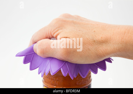 Die Hand der reifen Person, die ein Glas mit einem Silikonkautschuk-Untersetzer aufdreht, um den Deckel abzuziehen. England, Großbritannien Stockfoto