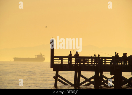 Menschen, die Angeln aus Dock von Burrard Inlet mit Frachter im Hintergrund, West Vancouver, Britisch-Kolumbien, Kanada Stockfoto