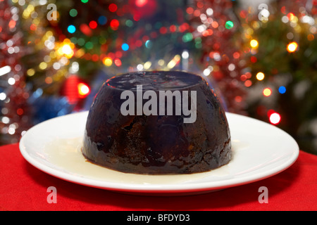 traditionellen Christmas Pudding mit Alkohol vor dem servieren auf dem Teller vor einem Weihnachtsbaum angezündet Stockfoto