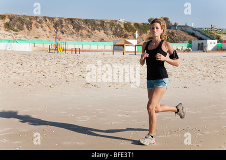 Junge Frau in ihren 20er Jahren joggt an einem Strand einen Musik-Player, befestigt an ihrem Arm - Model-Release verfügbar Stockfoto