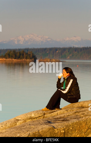Frau genießt ihren Kaffee morgens auf Klippen mit Blick auf die Georgia Strait auf Cortes Island Gulf Islands in British Columbia Kanada Stockfoto