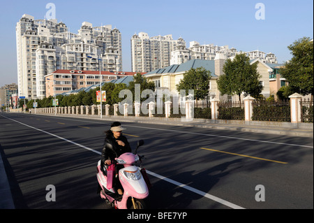 Lady Reiten Elektro Motorrad vorbei Verbindung der luxuriösen Apartments und Villen in Songjiang am Stadtrand von Shanghai 2009 Stockfoto