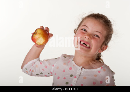 kleines Mädchen (7 Jahre alt), das vorderen Zähne Essen Apfel auf rote Bohnenbeutelstuhl gegen fehlt Stockfoto