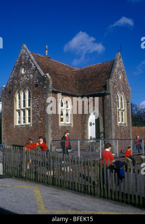 Chilham Kent UK. Typisch viktorianischen gotischen Dorf (Anfang der 1990er Jahre fotografiert) Schulkinder in roten Trikots auf Spielplatz Stockfoto