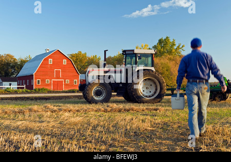 Bauer mit einem Lunchpaket zu Fuß in ein Feld von Getreide Stoppeln auf seinem Traktor, Grande Pointe, Manitoba, Kanada Stockfoto