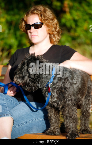 Schnauzer Mix Hund und Frau sind bei einem Außenbank im warmen Licht der Nachmittagssonne. Stockfoto