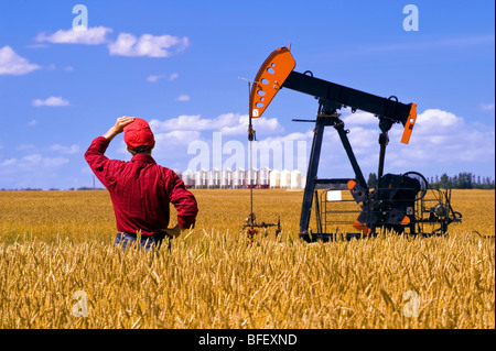 Man blickt auf eine Ernte bereit Weizenfeld mit einem Öl Pumpe Jack und Korn Lagerplätze im Hintergrund in der Nähe von Sinclair Manitoba Kanada Stockfoto