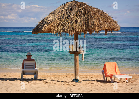 Strand-Szene: Mann sitzt am Sandstrand in Palm Dach Schatten; Korallenriffe, Atlantik, kubanische resort Stockfoto