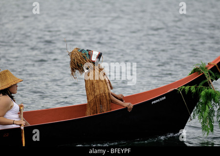 Native Mann sitzt am Bug des Kanus mit einheimischen Kopfschmuck im Tribal Journeys Ereignis am nordamerikanischen indigenen Spiele in Dun Stockfoto