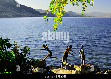 Statuen von Kindern spielen auf Felsen in der Nähe von Gewässerrand in Penticton, BC. Stockfoto