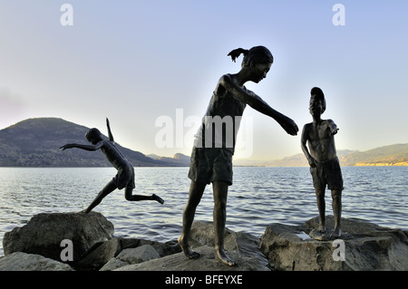 Statuen von Kindern spielen auf Felsen in der Nähe von Gewässerrand in Penticton, BC. Stockfoto
