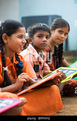 Indian School Kinder sitzen außerhalb ihrer Schule schreiben auf der Schiefertafel. Andhra Pradesh, Indien. Selektiver Fokus Stockfoto