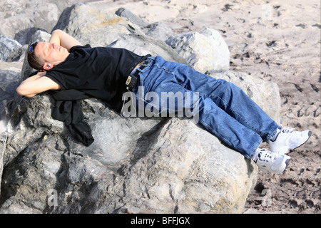 Man ruht auf Felsen am Strand, anhören von Musik über Kopfhörer, Long Island, NY Stockfoto