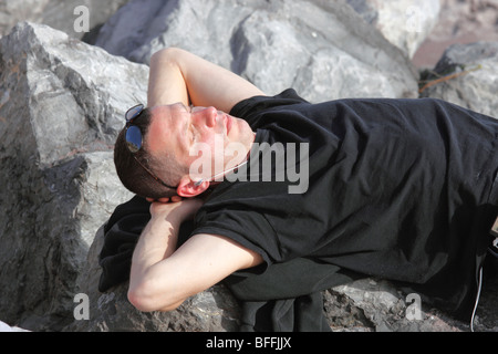 Man ruht auf Felsen am Strand, anhören von Musik über Kopfhörer, Long Island, NY Stockfoto