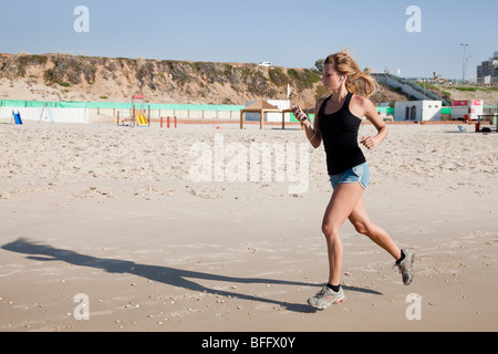 Junge Frau in ihren 20er Jahren joggt an einem Strand einen Musik-Player, befestigt an ihrem Arm - Model-Release verfügbar Stockfoto