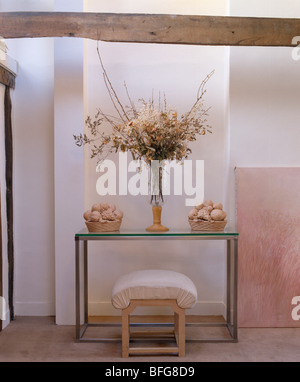 Blumenarrangement in hohen Vase auf modernen Glasplatte Tisch in traditionellen weißen Saal mit großen rustikalen Holzbalken Stockfoto