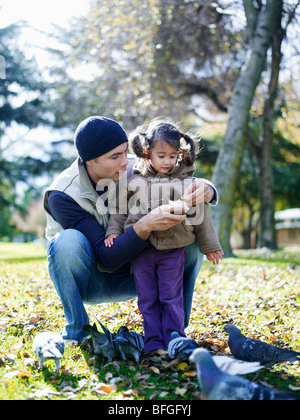 Mädchen (3-4) und Vater füttern Tauben im park Stockfoto