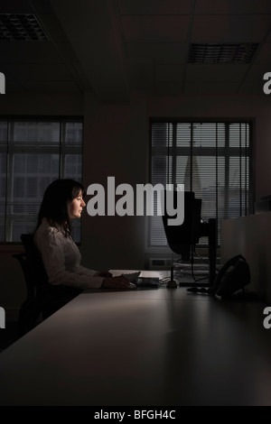 Weibliche Büroangestellte über Computer in abgedunkelten Büro, Seitenansicht Stockfoto