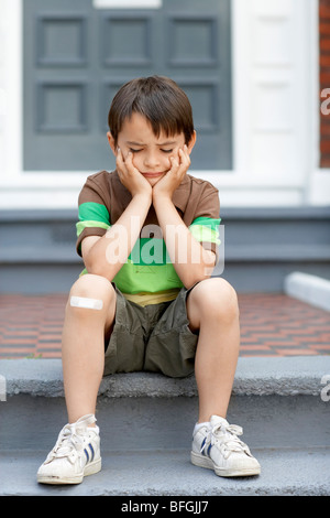 Trauriger kleiner Junge sitzt auf der Eingangstreppe des Hauses Stockfoto