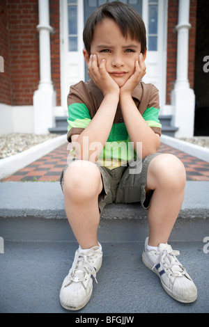 Trauriger kleiner Junge sitzt auf der Eingangstreppe des Hauses Stockfoto