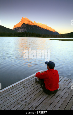 Erwachsene männliche sitzen auf dock Vermillion See bei Sonnenuntergang mit Mount Rundle im Hintergrund, Banff Nationalpark, Alberta, Kanada. Stockfoto