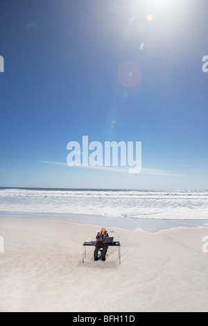 Senior Business-Mann am Schreibtisch sitzen, am Strand, erhöht, Ansicht Stockfoto