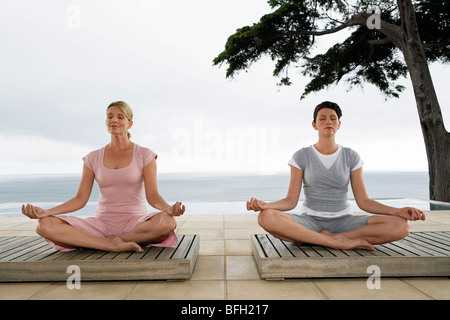 Zwei Frauen sitzen in Yoga-Positionen auf Terrasse Stockfoto