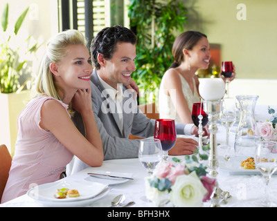 Junges Paar in der formalen Kleidung sitzen nebeneinander, Arme um am Tisch Stockfoto