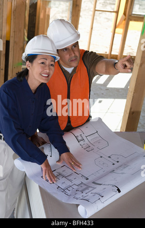 Architekten und Bau Arbeiter blickte zu Decke mit Blaupausen auf Tisch innen Hälfte gebaut Haus Stockfoto