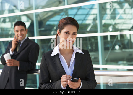 Geschäftsfrau mit PDA mit Geschäftsmann mit Handy im Hintergrund, im freien Stockfoto
