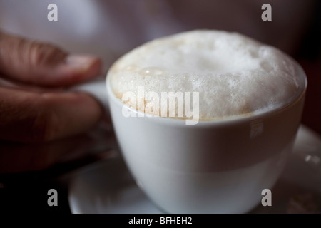 eine Hand hält eine Tasse Cappuccino hautnah Stockfoto