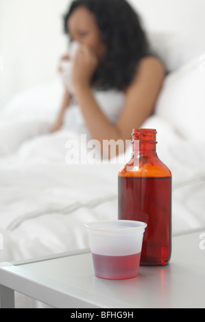 Medizin auf Nachttisch neben Frau im Bett Stockfoto