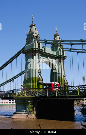 Einzelne rote Londoner Doppeldeckerbus kreuzt Hammersmith Bridge an einem sonnigen Sommertag. Stockfoto