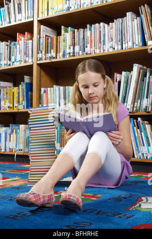 Mädchen auf dem Boden sitzend und Buch in Bibliothek Stockfoto